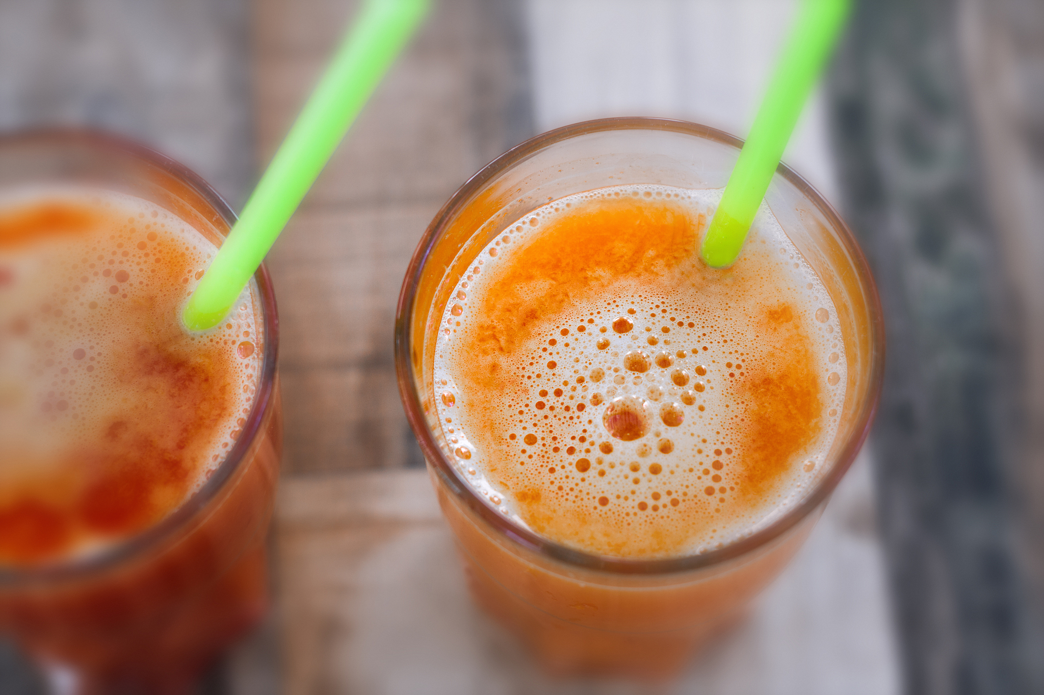 two bright glasses of fresh-pressed orange juice, green straws