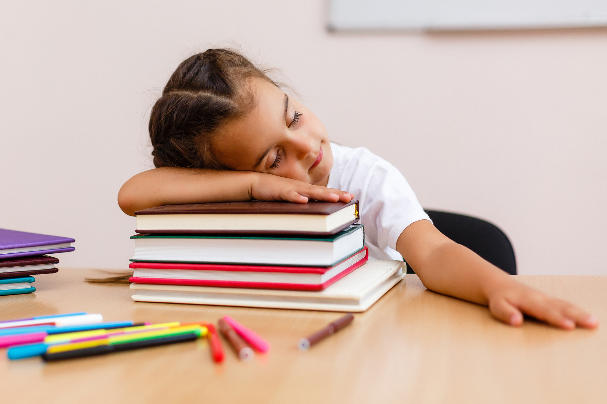 adorable little girl sleeping on a stack of books over white bac