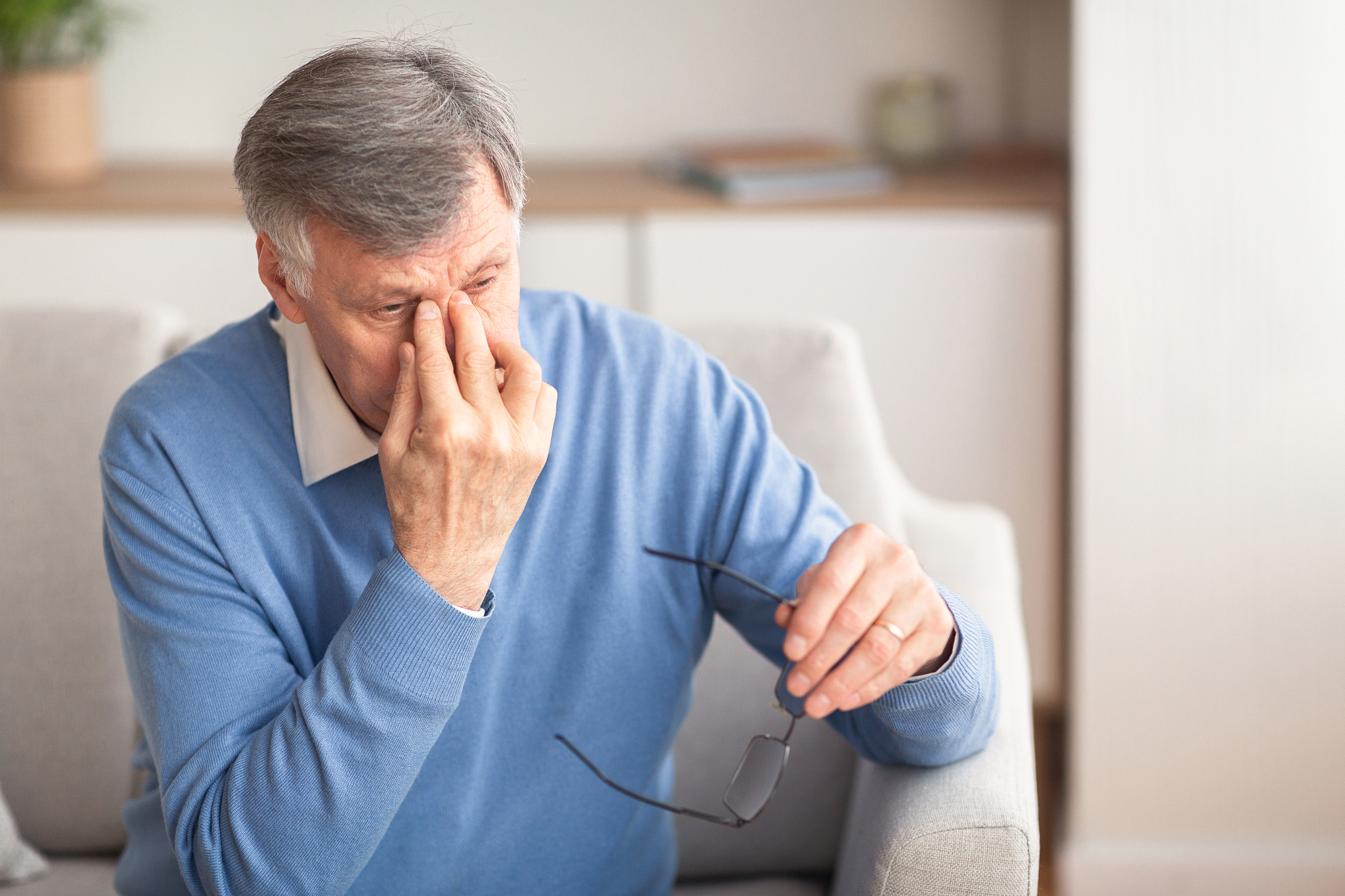 senior man massaging nosebridge sitting on sofa, selective focus
