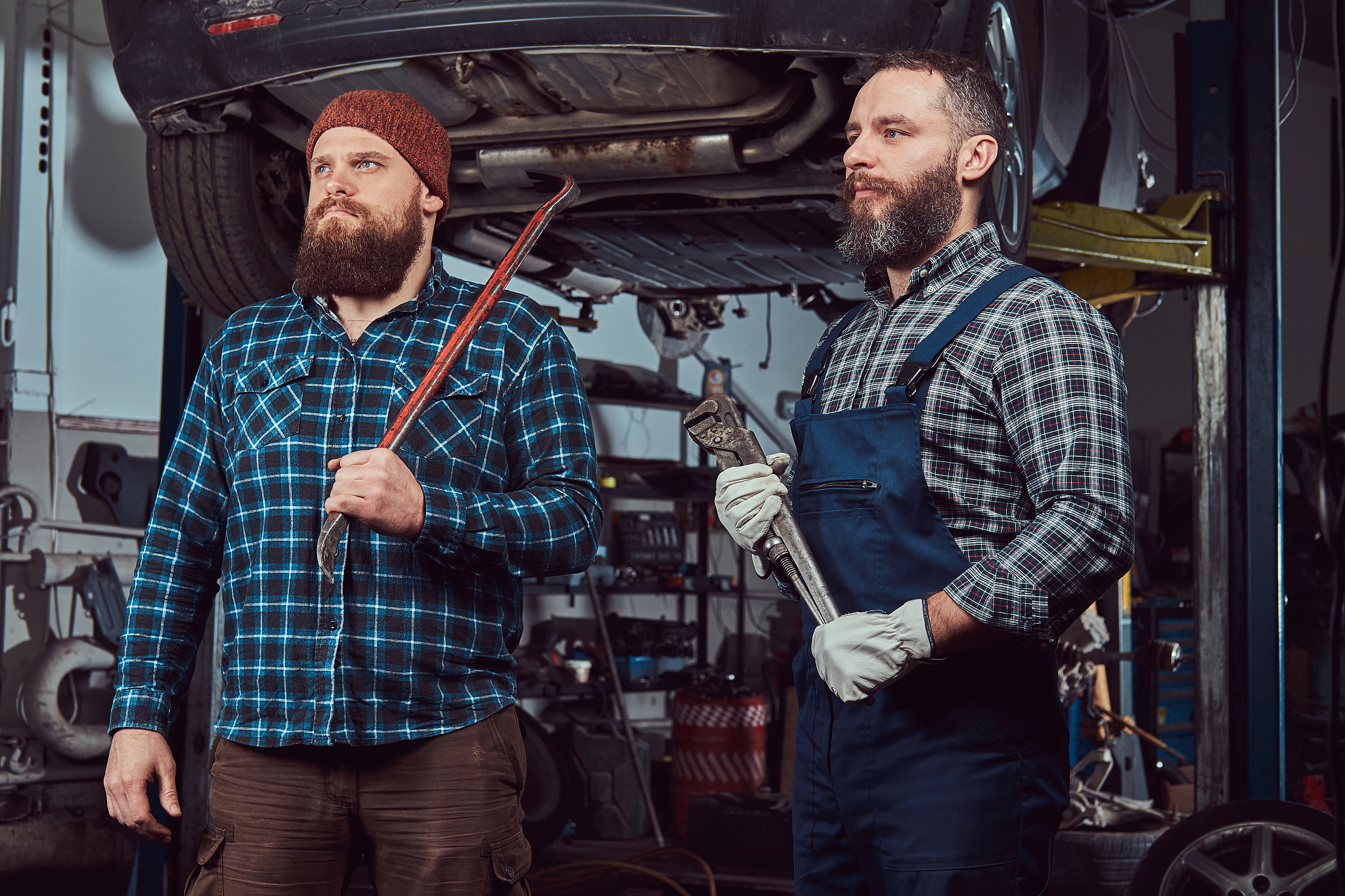 two bearded brutal mechanics repair a car on a lift in the garag