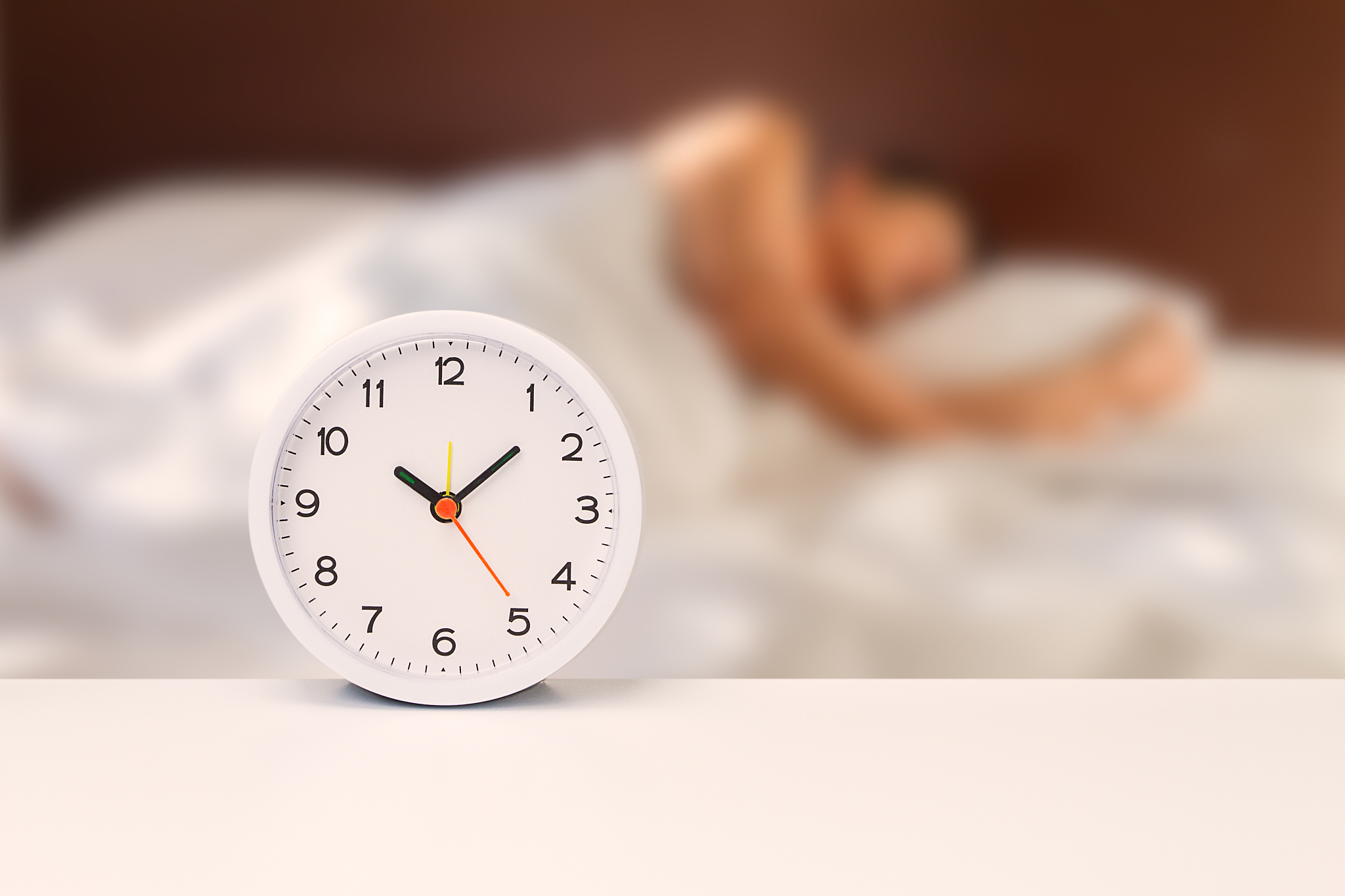 white alarm clock on white desk on blurred man sleeping on white