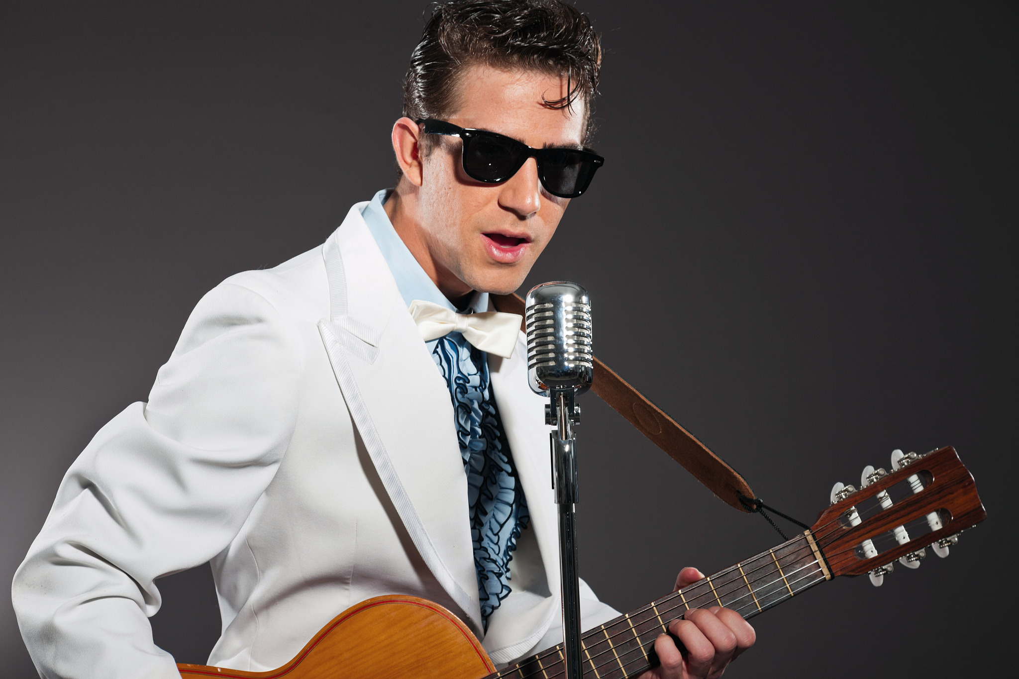 retro rock and roll singer with guitar wearing white suit.