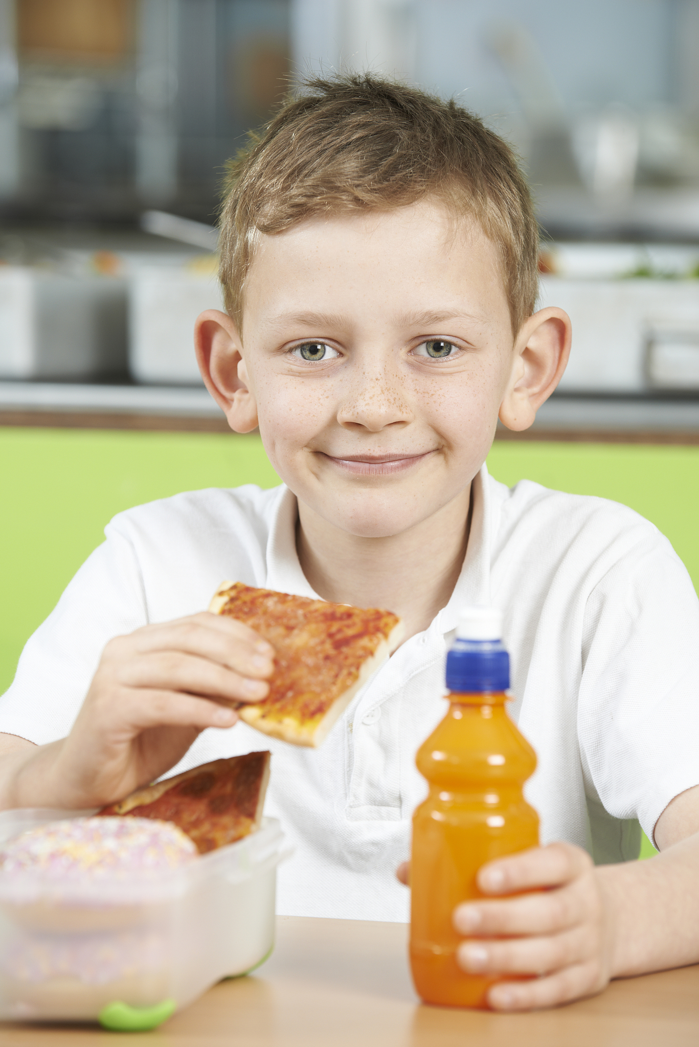 male pupil sitting at table in school cafeteria eating unhealthy
