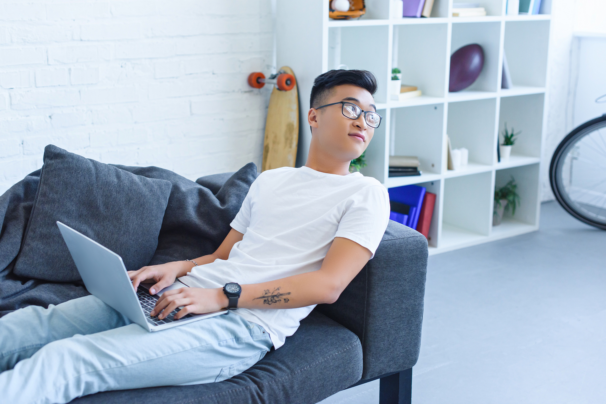 handsome asian man using laptop on sofa at home and looking away