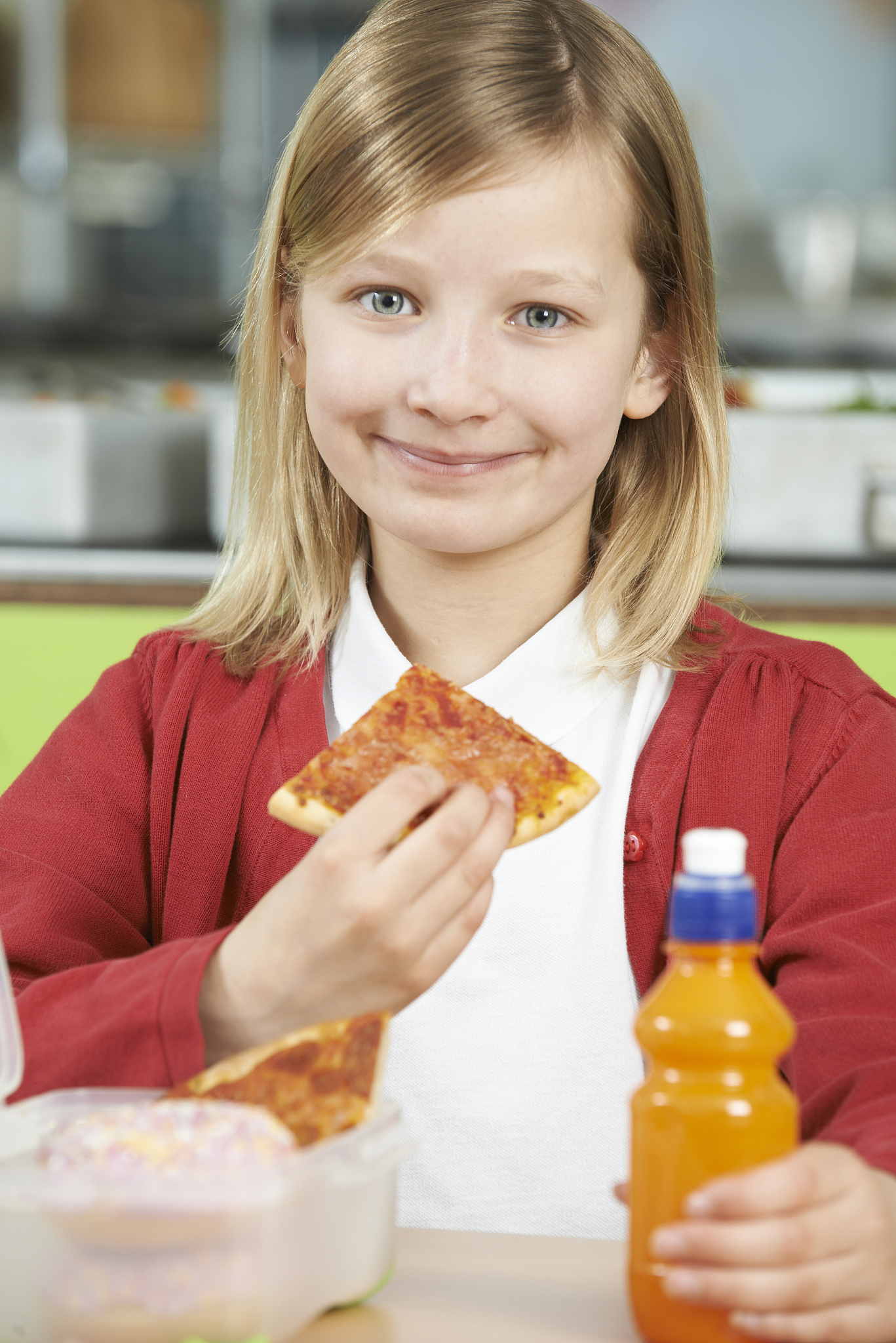 girl sitting at table in school cafeteria eating unhealthy packe