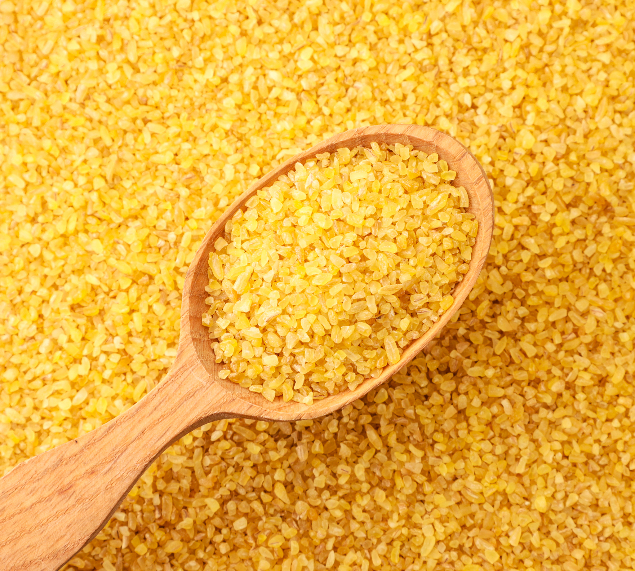dry bulgur in a wooden spoon on a background of cereals. the vie