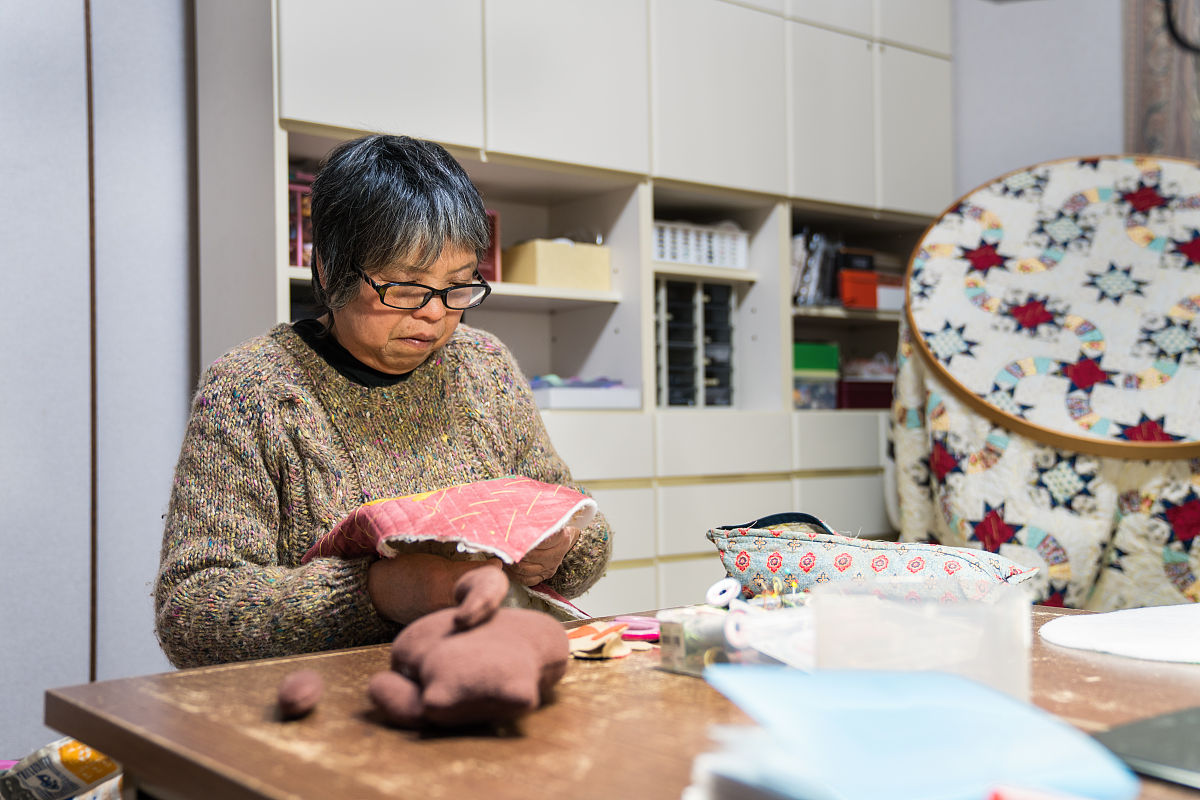 一位年长妇女在她的家中缝纫和制作工艺品