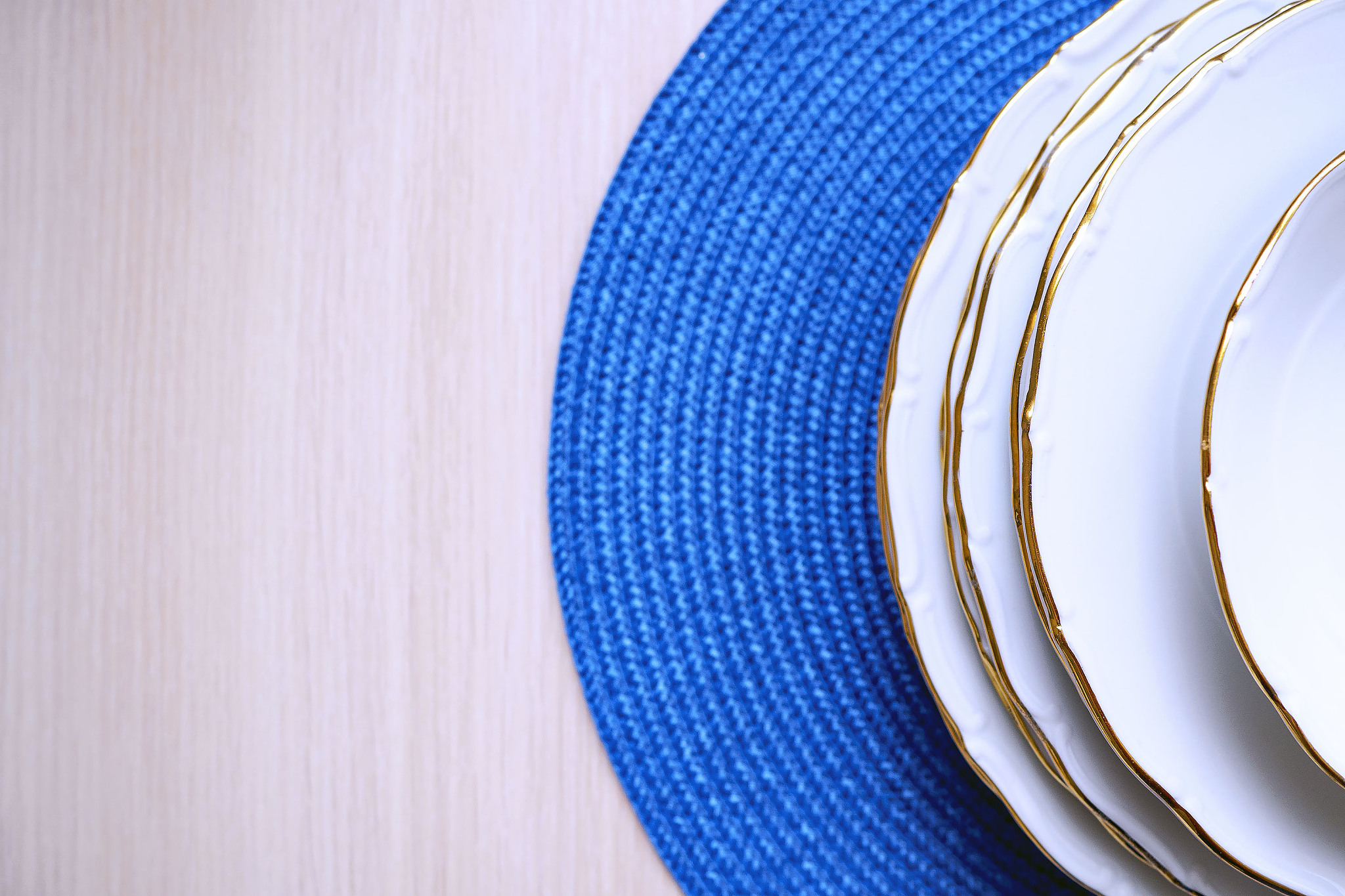 top view of white plates with gold rim on blue woven mat and on 