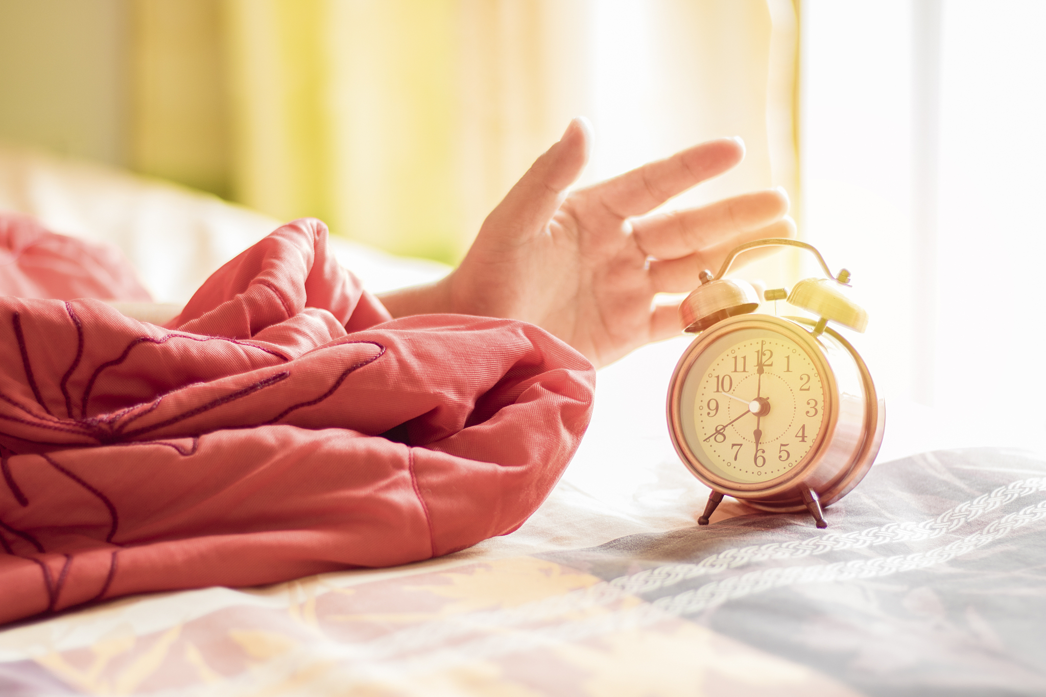 cropped hand of person reaching alarm clock on bed at home