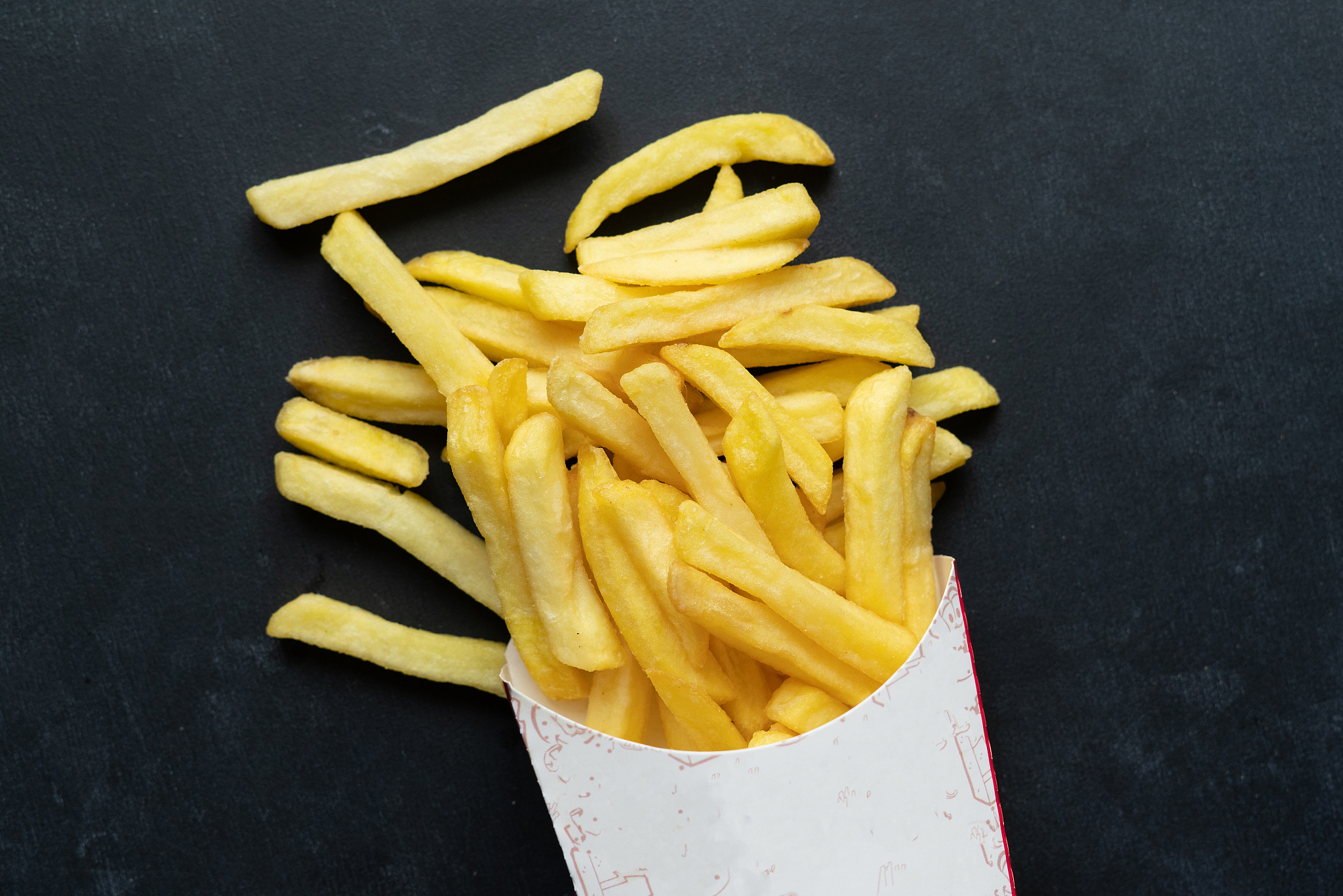 fresh fried junk potato fries come out from the paper box on col