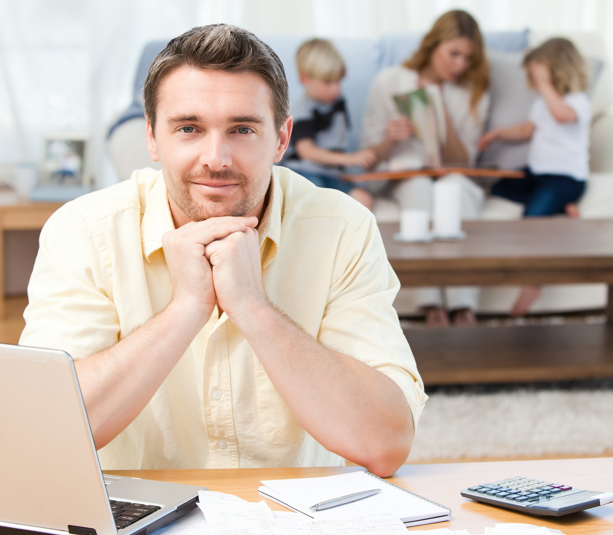 man calculating his bills while his family is on the sofa