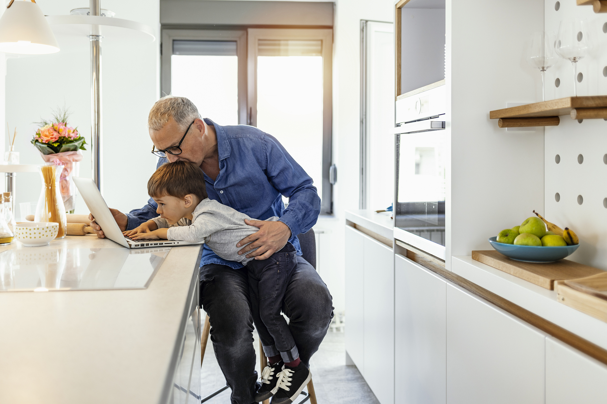 father working on laptop and holding son on his lap