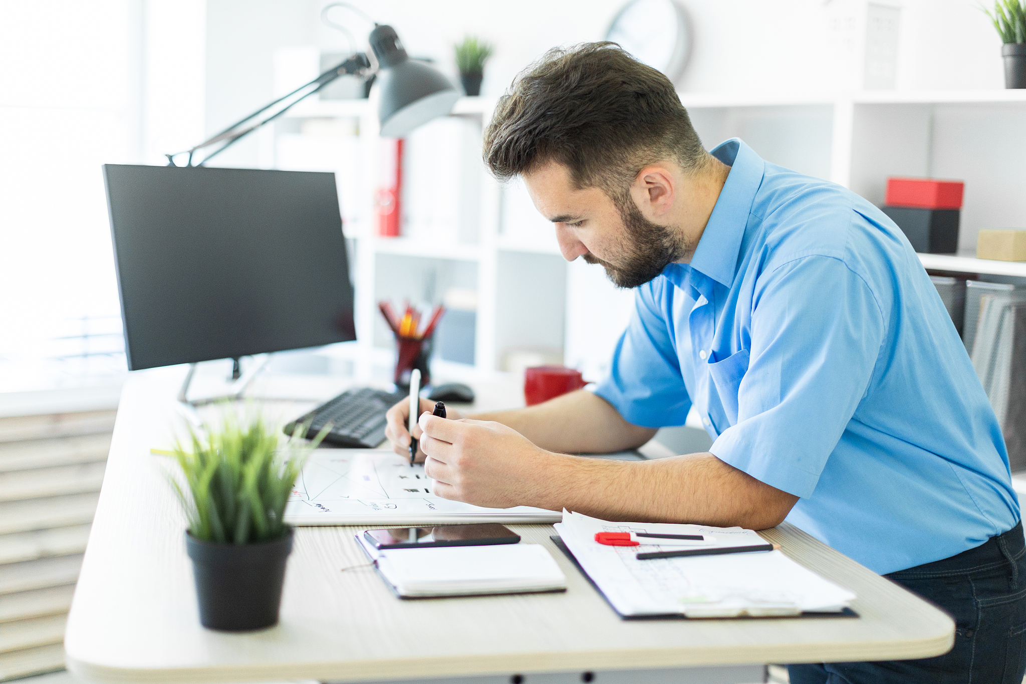 a young man standing in the office at a computer desk and workin