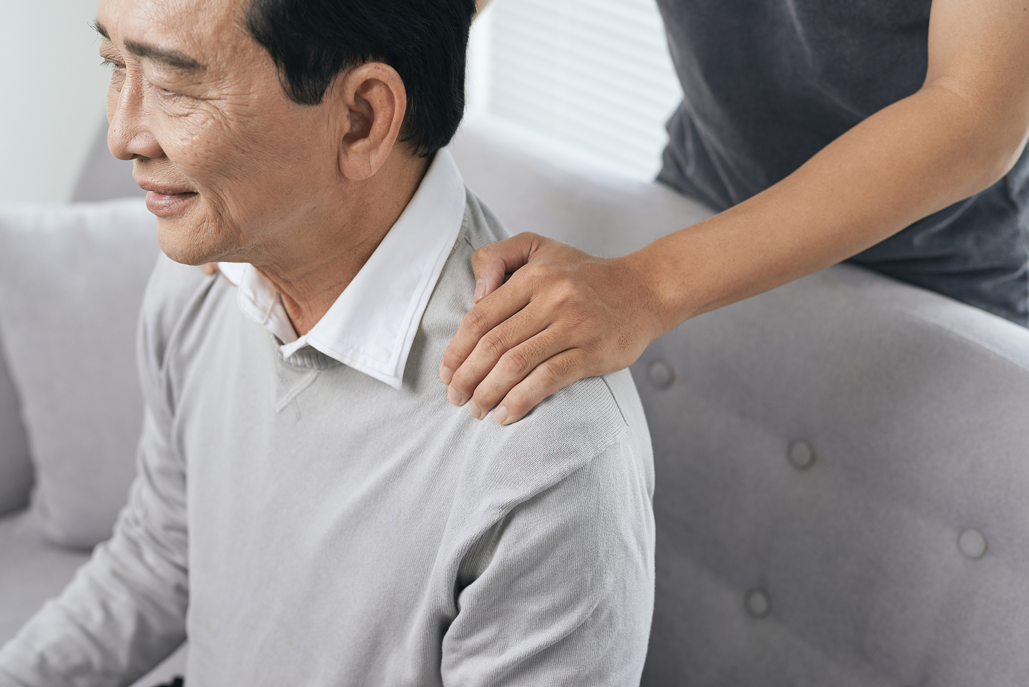 asian old man shoulder pain, sitting on sofa , son massaging fat