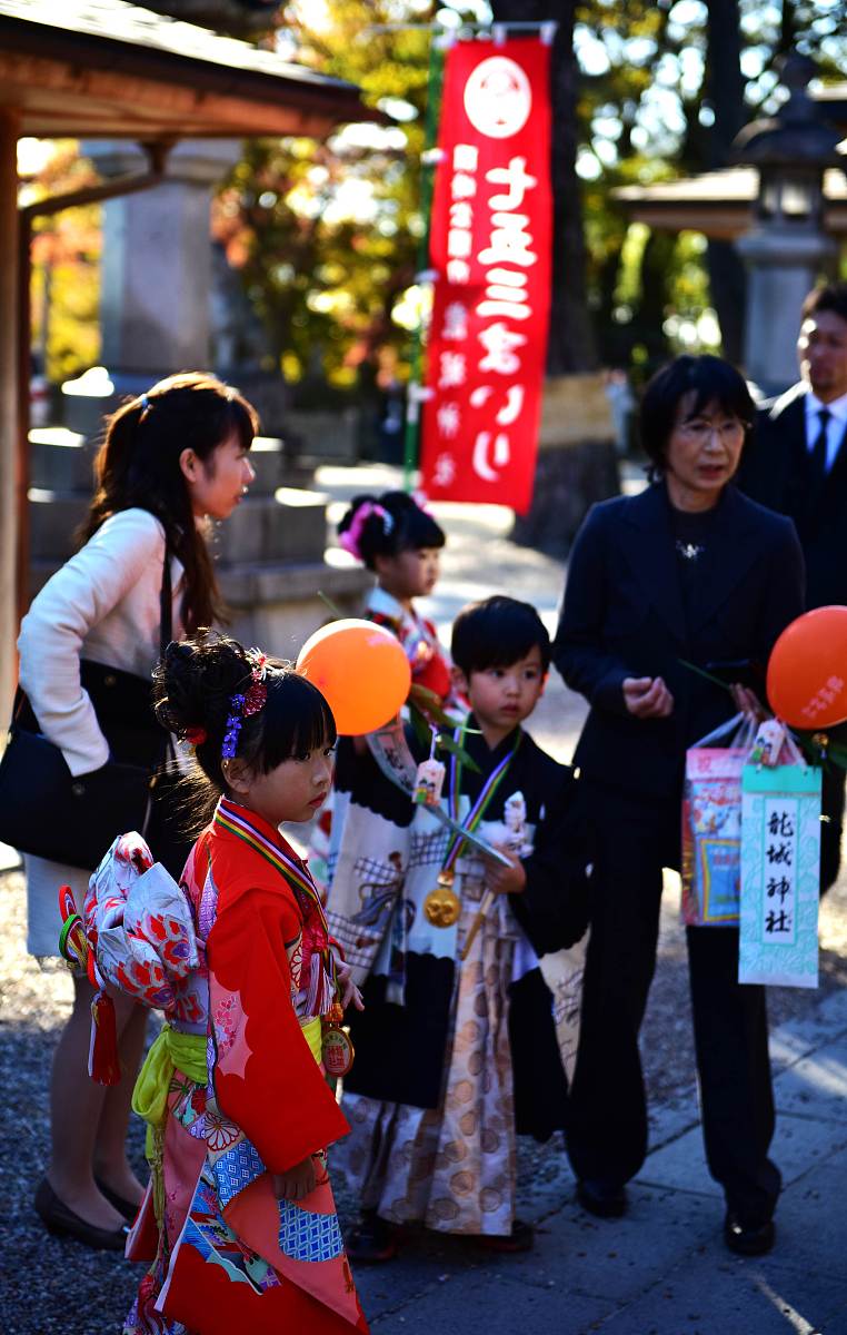 请描写一下一个老婆婆带着1一个年轻人和一个小孩儿在神社参拜一个女巫然后去偏殿吃了一些东西就下山回家的画面