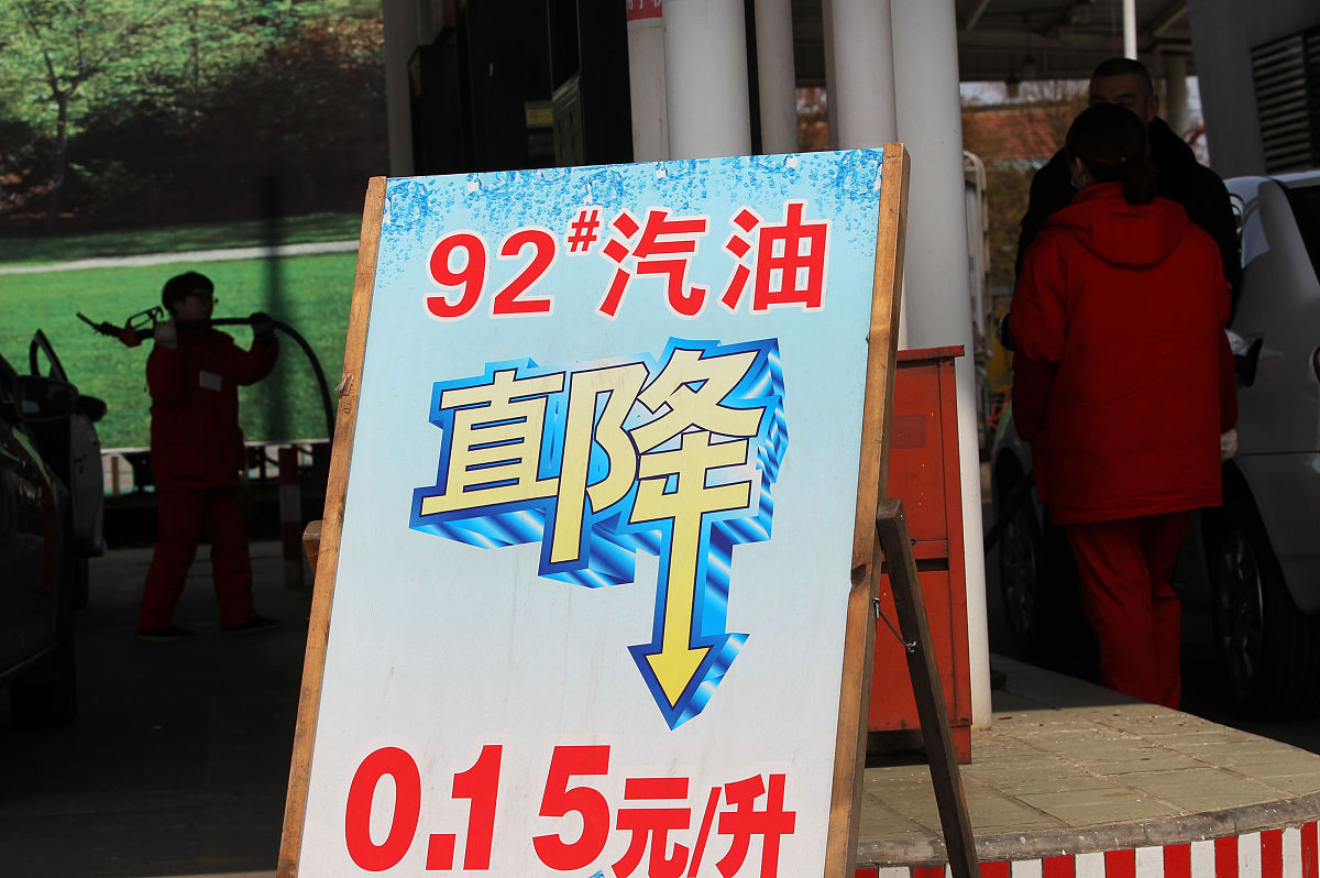 2015年3月24日,江苏南通,加油站工作人员在降价牌子旁为车辆加油.