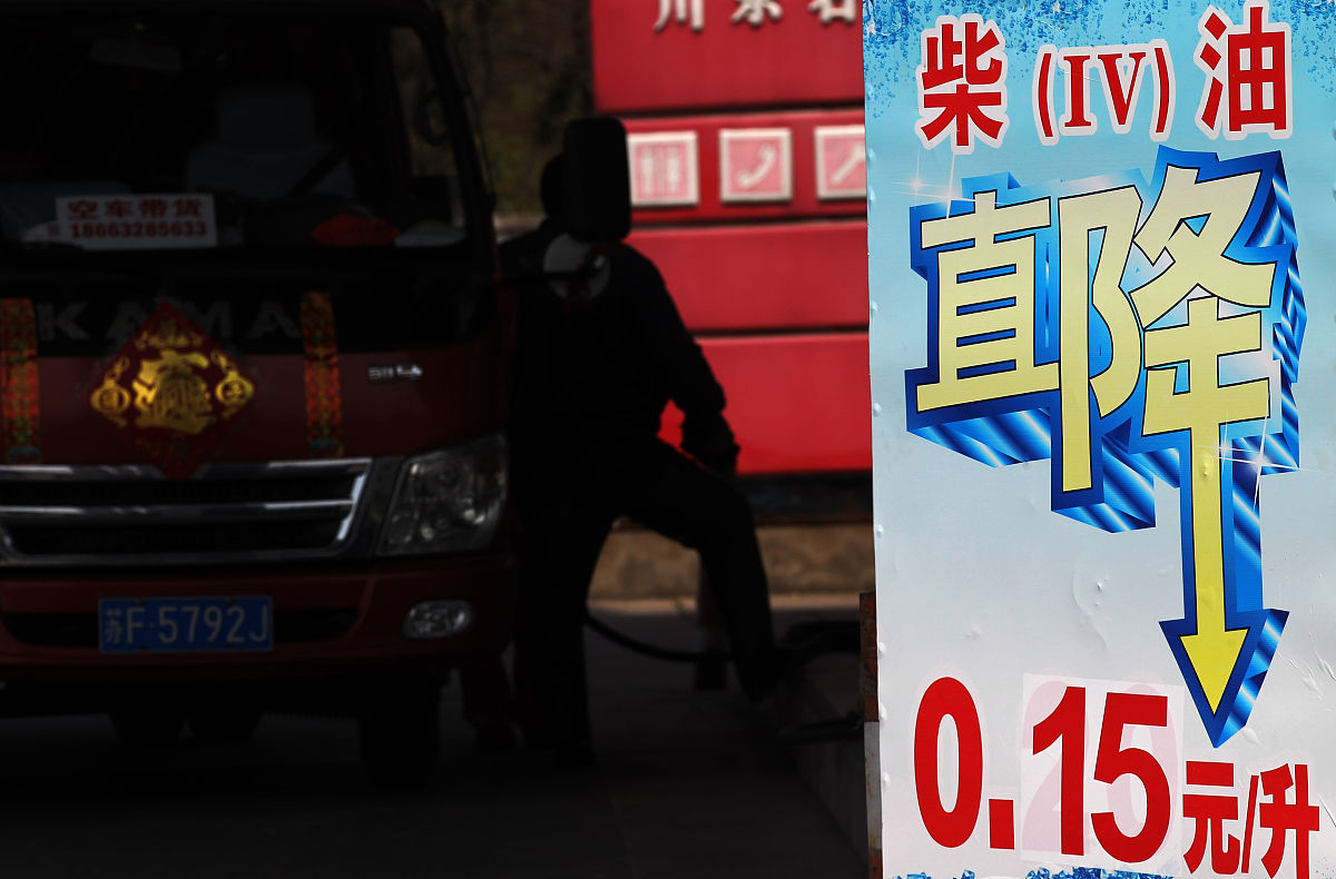 2015年3月24日,江苏南通,加油站工作人员在降价牌子旁为车辆加油.