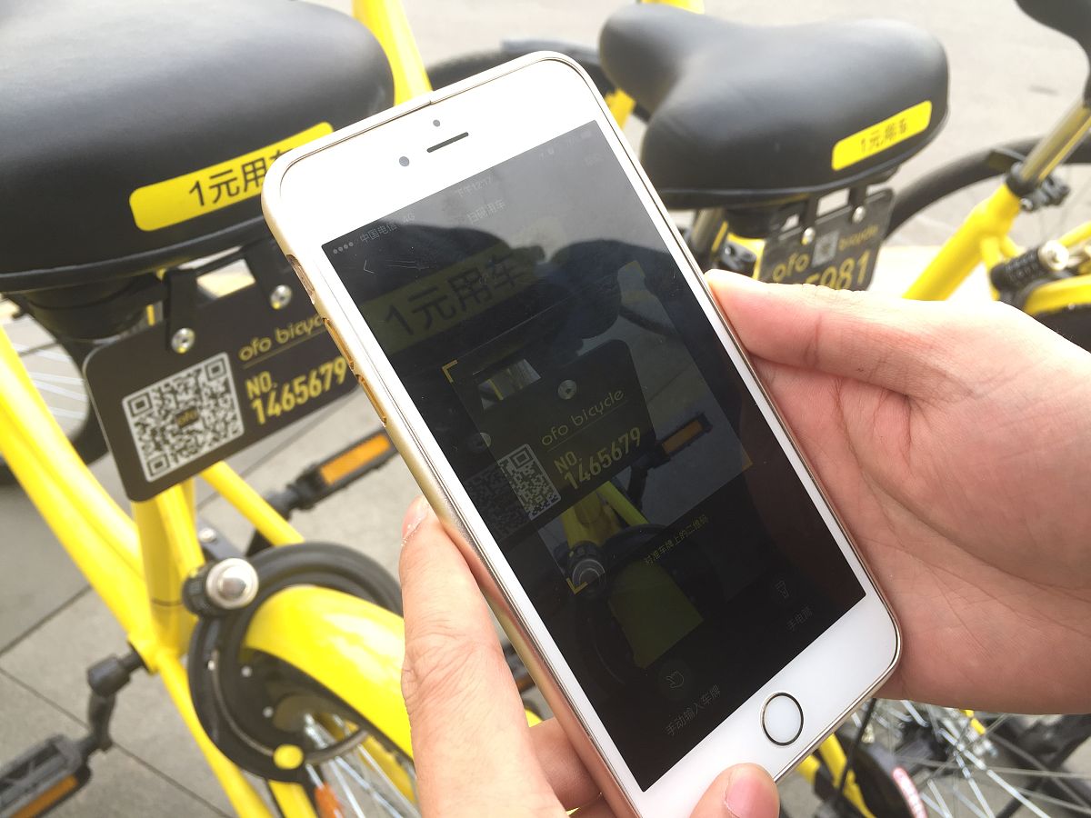 Two Women Scanning Shared Bikes with Smartphones in a Bustling City