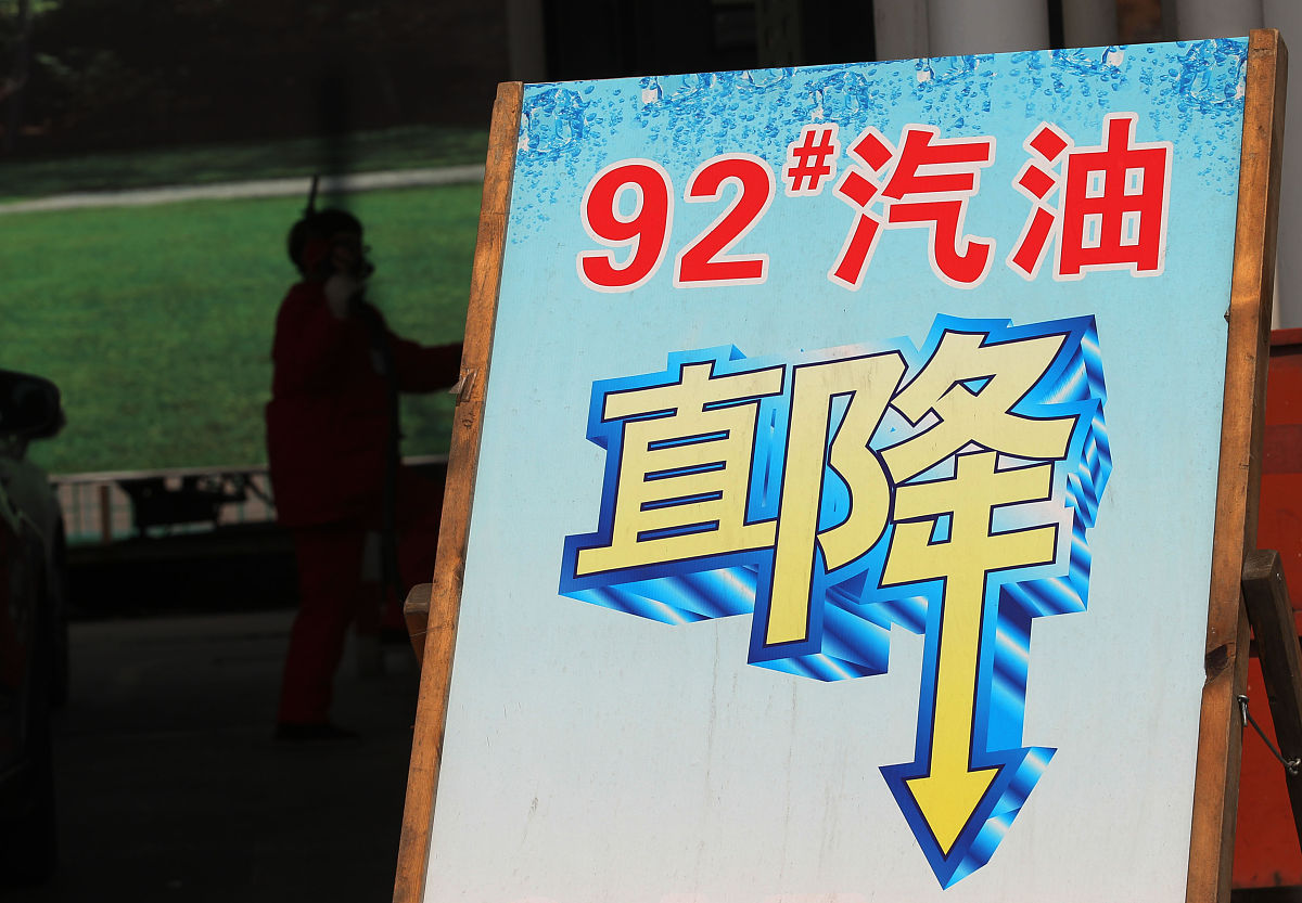 2015年3月24日,江苏南通,加油站工作人员在降价牌子旁为车辆加油.