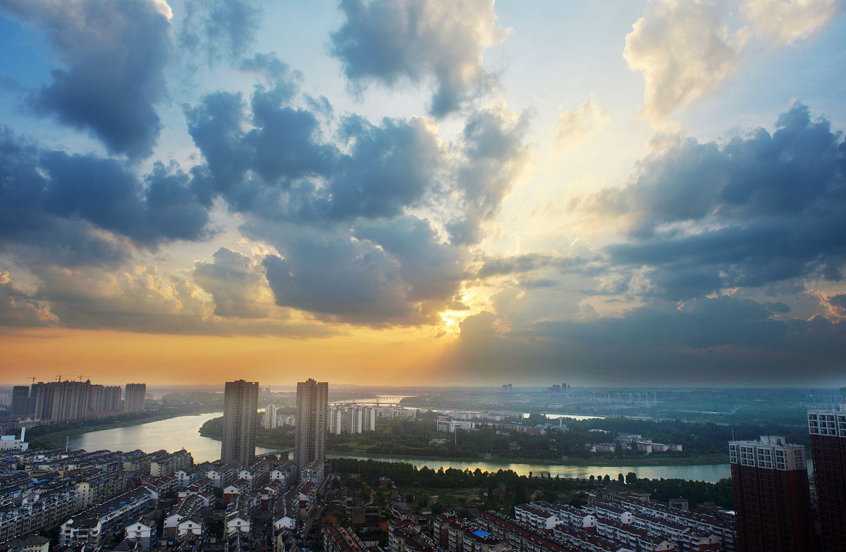 2019年7月26日黄昏,安徽六安,夕阳余晖穿透云层,映照在绿水环绕的月亮