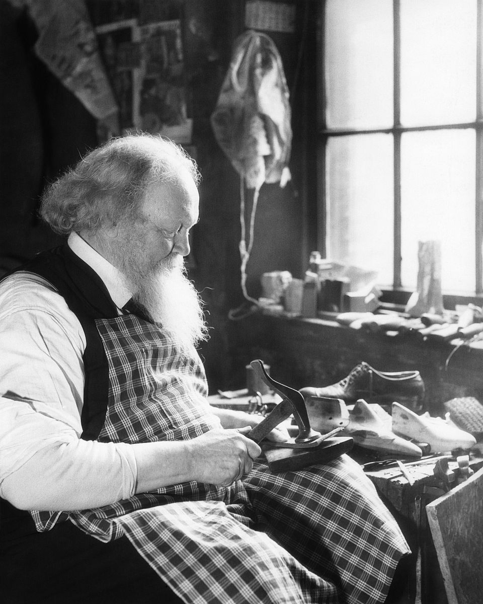 1920s 1930s bearded elderly cobbler by window at workbench repai