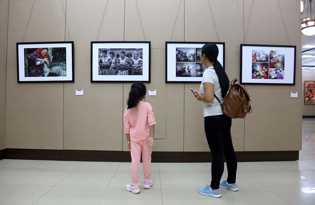 2017年9月7日,沈阳.一家长带孩子在少数民族美术书法摄影展上观看作品