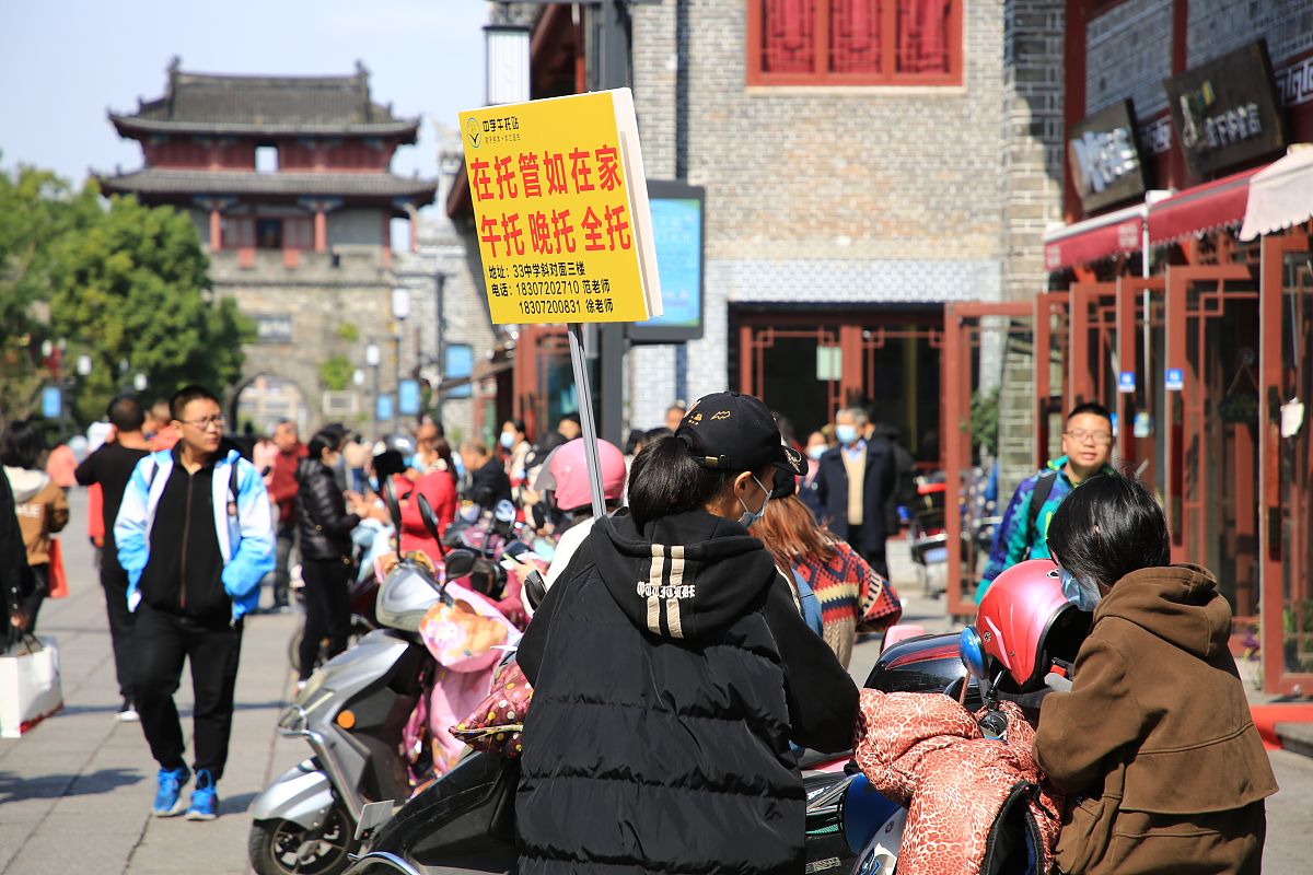 2021年10月21日,湖北省襄阳市,一名校外托管站工作人员举着牌子向家长