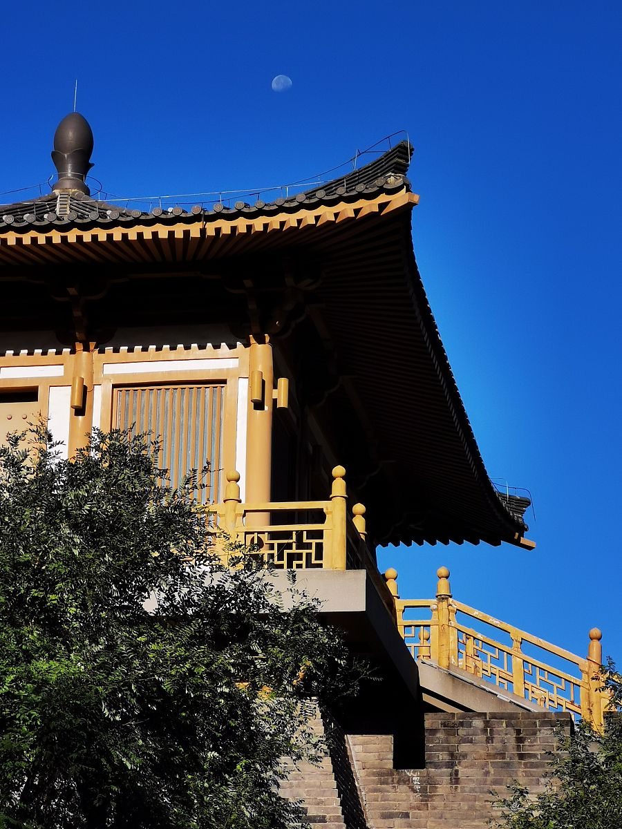 2021年8月27日晨曦,西安市曲江唐城墙遗址公园的古建筑在一轮秋月蓝天