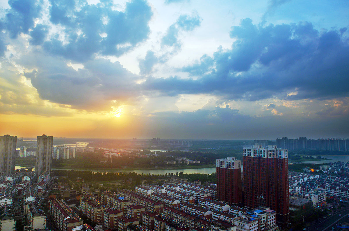 2019年7月26日黄昏,安徽六安,夕阳余晖穿透云层,映照在绿水环绕的月亮