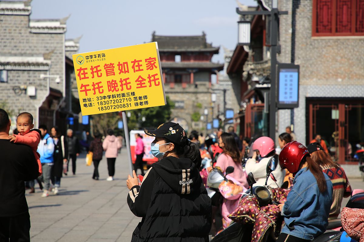 2021年10月21日,湖北省襄阳市,一名校外托管站工作人员举着牌子向家长