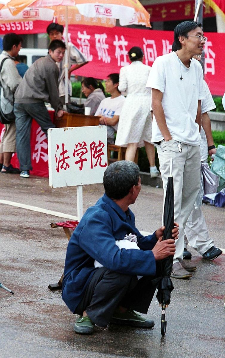 一个来自农村的大学新生父亲蹲在"法学院"报到处的牌子前看一个高年级