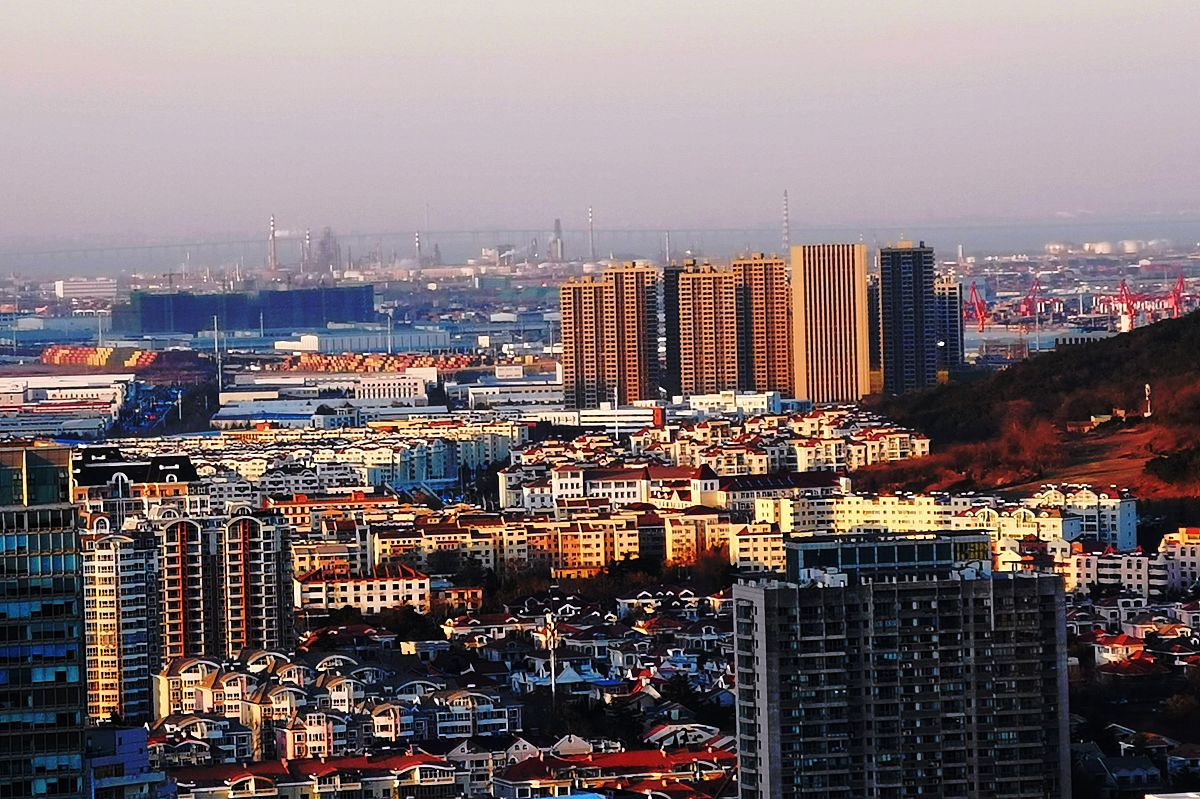 2021年12月3日,山东青岛,西海岸新区海滨与城市被笼罩在一片暖橙色的