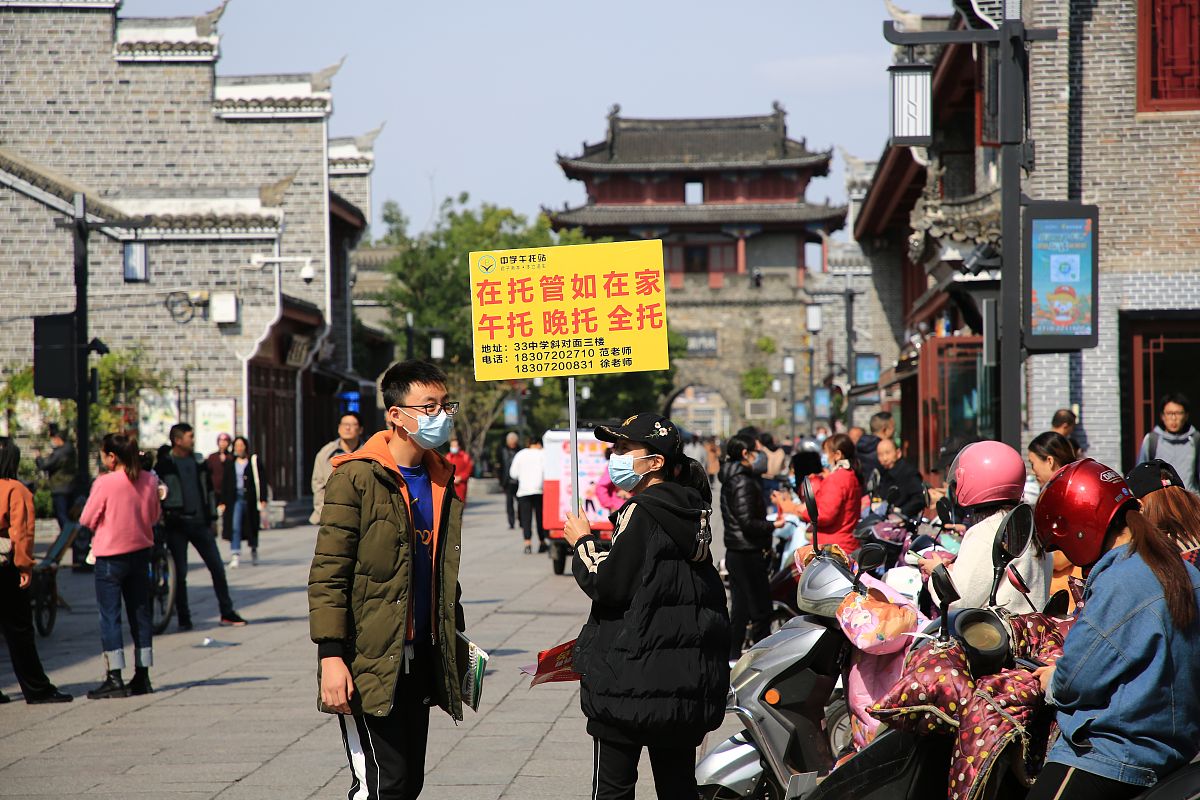 2021年10月21日,湖北省襄阳市,一名校外托管站工作人员举着牌子向家长