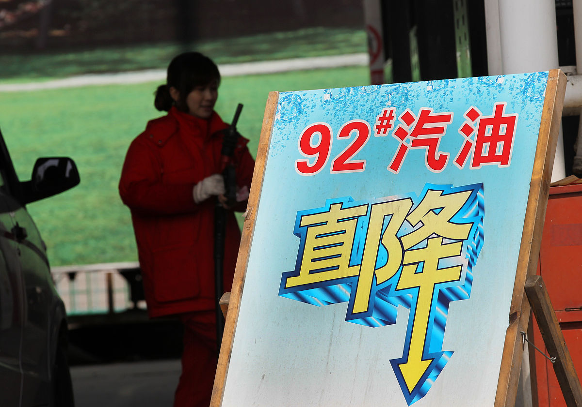2015年3月24日,江苏南通,加油站工作人员在降价牌子旁为车辆加油.