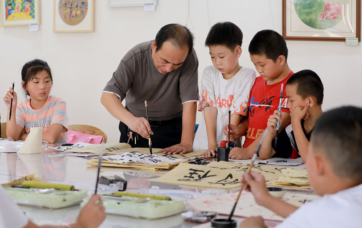 2021年8月3日,四川省华蓥市,一名书法老师在教青少年儿童写毛笔字.
